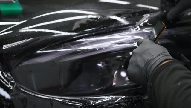 Using a scraper to put on tinting film on car headlights. Car detailing concept. High quality 4k footage