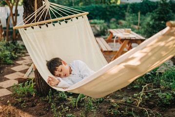 Kid child boy having rest sleep in hammock at country house cottage yard garden outdoors at spring...