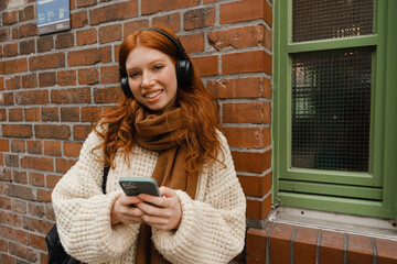 Smiling redhead girl using mobile phone while standing outdoors
