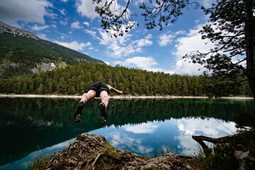Fototapeta na wymiar Guy jumping into Lake Blindsee with the Alps in the background, Tyrol, Austria