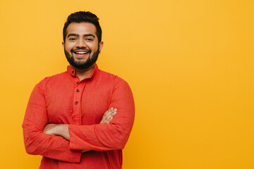 Young indian man smiling while standing with folded arms isolated over yellow background