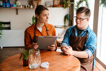 Female with clipboard training man with down syndrome to work in cafe while sitting at table