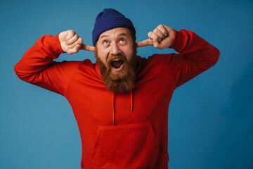 Fototapeta premium Annoyed man screaming and covering his ears isolated over blue wall