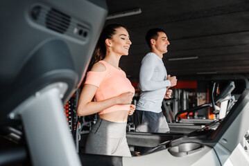 Sporty happy couple running together on treadmills at the gym.