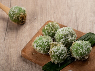 Indonesian traditional cake Klepon is served on a wooden tray. It's a boiled rice cake stuffed with...