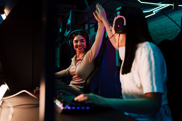 Two excited girls giving high five to each other while playing online video game in cybersport club © Drobot Dean