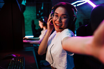 Smiling asian girl taking selfie while playing online video game in cybersport club