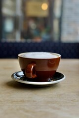 A cup of frothy cappuccino on a wooden table in a coffee shop