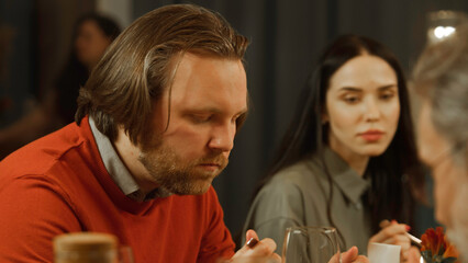 Close up shot of man eating delicious dish, smiling, talking with friends in modern gastro cafe. He has birthday party, family dinner, spends evening in restaurant. Concept of public eating. Zoom in.