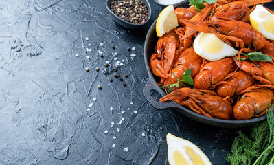cooked crawfish in black saucepan with lemons and spices on dark background