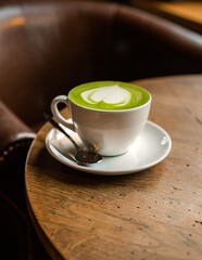 cup of coffee on the wooden table, in the cafe, green matcha , white cup on the table, hot beverage