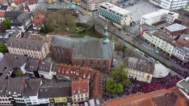 Aerial rising up tilting down, FCK Football audience fans crowd celebrating win at the bars of old city in Kaiserslautern Germany.
street intersection and Romanesque-Gothic-style church in Background