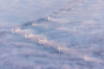 Windmills, windturbines above of the fog clouds in morning light