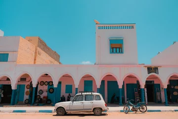 Tischdecke Mirleft, Morocco - colorful market exterior with blue doors and windows, pink walls, white arches. Vintage vehicles parked outside: a white Renault 4 and an old blue motorcycle. Spanish architecture. © pam
