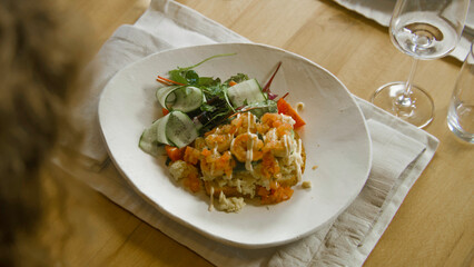 Close up shot of waiter bringing plate with delicious dish to guest. Toast with scramble, shrimps, sauce and green salad stands on the table in restaurant with modern cuisine. Public eating concept.