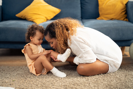 mother is taking care of her daughter by covering a wound or scrape on her knee with a plastic bandage to help reducing the risk of infection and allowing the wound to heal more quickly.