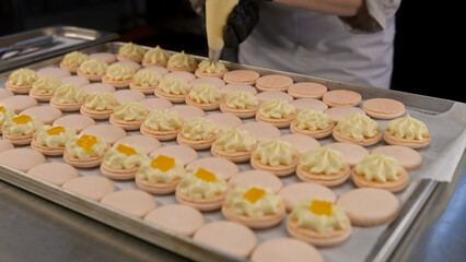 Professional confectioner squeezes ganache cream on macarons shells by piping bag and makes final touches. Process of making delicious french dessert. Concept preparation of confectionery and baking.