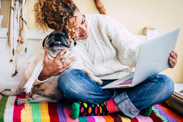 Dog lover hugging her puppy sitting on a bench and surfing the net on laptop with wireless...