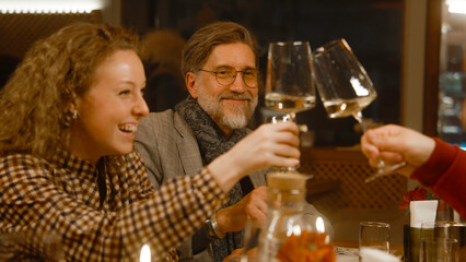 Group of people sit in modern gastro cafe, clink glasses, drink wine and talk at dinner. Friends spend free time or weekend evening, hangout on birthday party in restaurant. Concept of public eating.