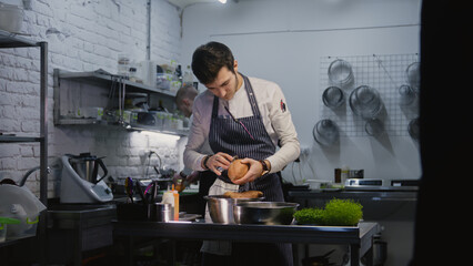 Adult cook in apron cleans up working desk and peels sweet potato for future dishes. Professional chefs preparing vegetables and making food. Concept of teamworking in restaurant kitchen. Slow motion.