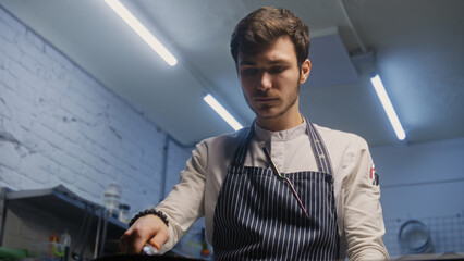 Chef cooks delicious meal on stove. Male cook fries meat on frying pan, turns it on other side,...