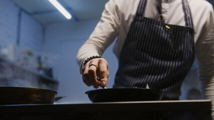 Male cook in apron fries and stirs juicy meat in frying pan over stove. Process of preparing gourmet dish. Restaurant with professional cuisine. Meal making concept. Public catering. Gastronomic art.