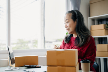 adult woman start up small business owner writing address on cardboard box at workplace.small business entrepreneur SME or freelance, female working with box at home.