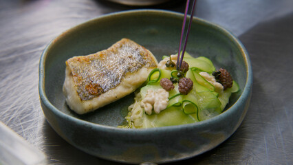 Male cook decorates dish for serving. The chef makes presentation of dish with fried fish and steamed vegetables, puts berries on top. Restaurant with professional gourmet cuisine. Public catering.