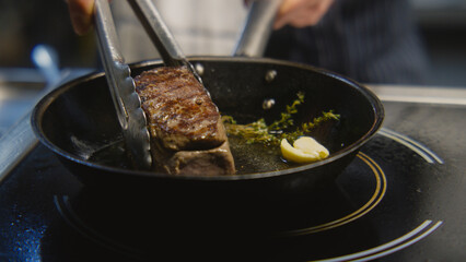 The chef cooks delicious meal on stove. The cook fries piece of juicy pork meat on frying pan with...