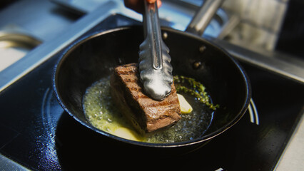 The chef cooks delicious meal on stove. The cook fries piece of juicy pork meat on frying pan with...