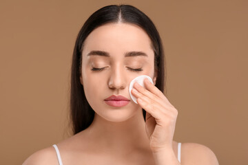 Beautiful woman removing makeup with cotton pad on beige background