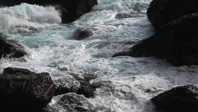 Slow motion. Brightly turquoise waves break into white foam on the coastal cliffs and seethe between them. The need to protect the environment. Ecology and global warming.