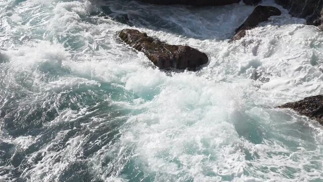 Brightly turquoise waves break into white foam on the coastal cliffs and seethe between them, sparkling in the rays of the summer sun. Tourist attraction. Itinerary for hiking on a weekend or holiday