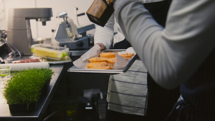 Male cooks make tasty meal. They add salt or spices into sweet potato on baking sheet using spice grinder before baking it in oven. Process of cooking. Restaurant with gourmet cuisine. Slow motion.