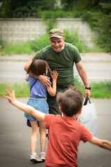 Military man in olive uniform and cap meeting and hugging his kids and smiling outdoors in summer