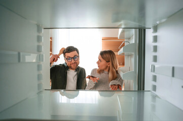 Woman is complaining about an empty fridge to her husband on the kitchen