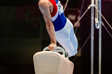 male gymnast performing on pommel horse competition artistic gymnastics in background ring frame...