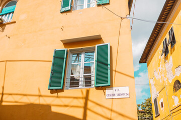 Windows on yellow painted facade of the house. Window with green shutters on a yellow house. Colorful architecture in Pisa, Italy.