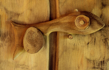 Door wooden handle in the shape of a fish on light wooden doors, close-up