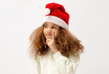 A beautiful and cute girl in a santa claus hat isolated on a white background shows emotions, the concept of the new year and christmas.