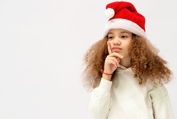 A beautiful and cute girl in a santa claus hat isolated on a white background shows emotions, the concept of the new year and christmas.