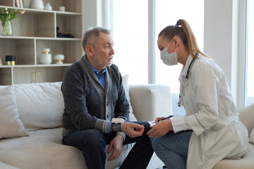 Female doctor senior man taking his blood pressure in doctor office or at home. Old man patient and doctor have consultation in hospital room. Medicine healthcare medical checkup. Visit to doctor