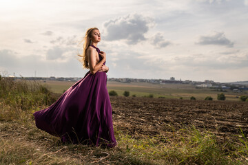 Caucasian blonde woman wearing a purple dress posing in a wild nature