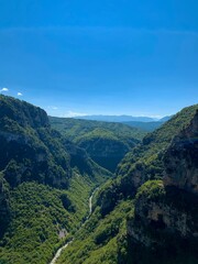 Fototapeta premium Vikos gorge, panoramic view of forestеd slopes, massive limestone cliffs, Voidomatis riverbed bends, and distant Pindus mountain randes from Beloi Viewpoint. Vikos-Aoos National Park, Zagori, Greece.