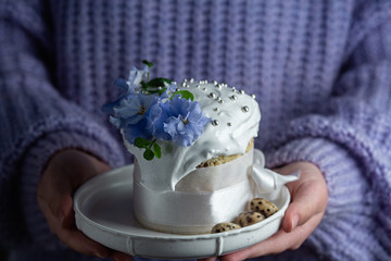 A woman holds in her hands an Easter cake with meringue and decor in a plate