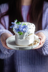 A woman holds in her hands an Easter cake with meringue and decor in a plate