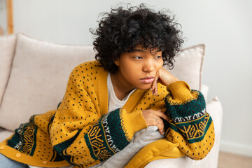 African american sad thoughtful pensive unmotivated girl sitting on sofa at home indoor. Young...