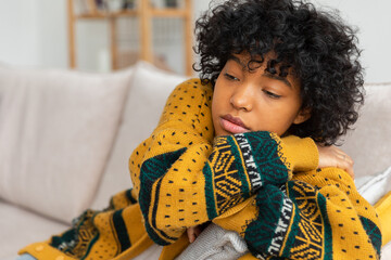 African american sad thoughtful pensive unmotivated girl sitting on sofa at home indoor. Young african woman ponder look tired after long day. Girl feels depressed offended lonely upset heartbreak