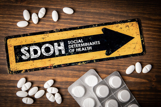 SDOH Social Determinants Of Health. Yellow direction sign with text and pills on wooden background
