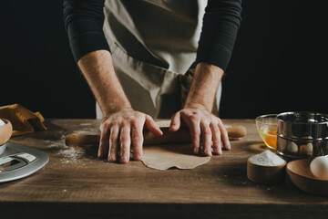 Unrecognizable man rolling out the dough with a rolling pin on wooden background